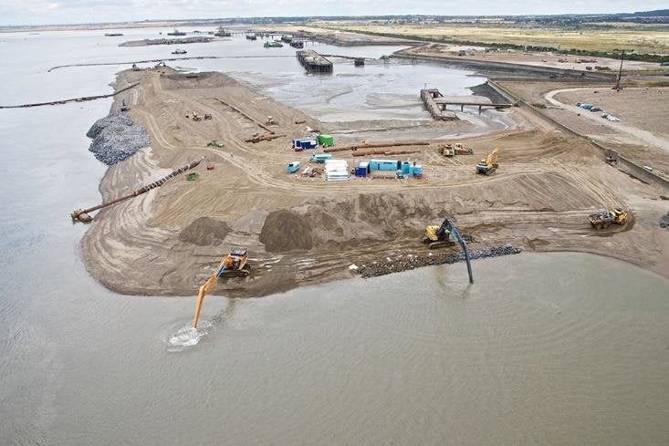 Dredger discharging fill on a reclamation site, with excavators shaping the new shoreline